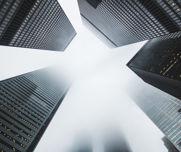 A shot from below of skyscrapers disappearing into fog.