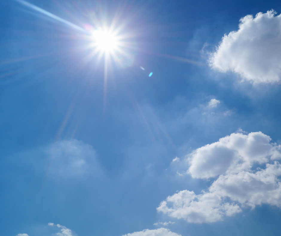 The sun shining brightly in the blue sky among clouds.