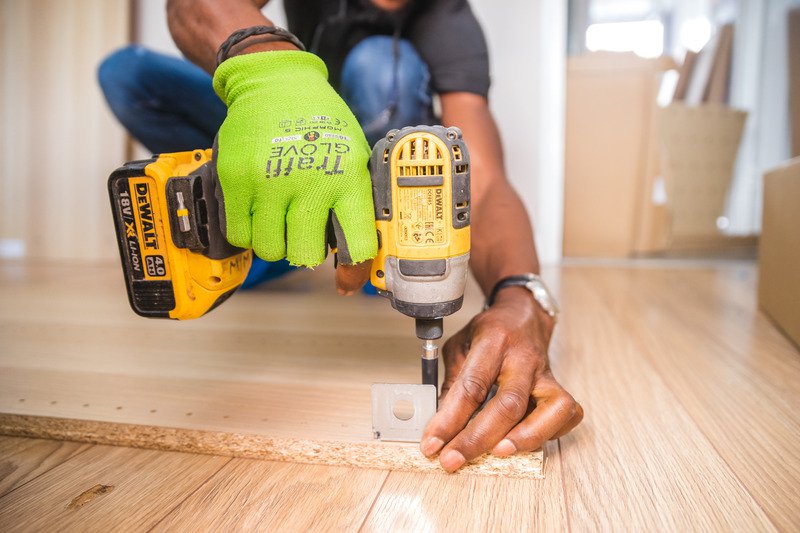 A person drilling with a yellow and black drill, wearing a pair of bright green safety gloves.