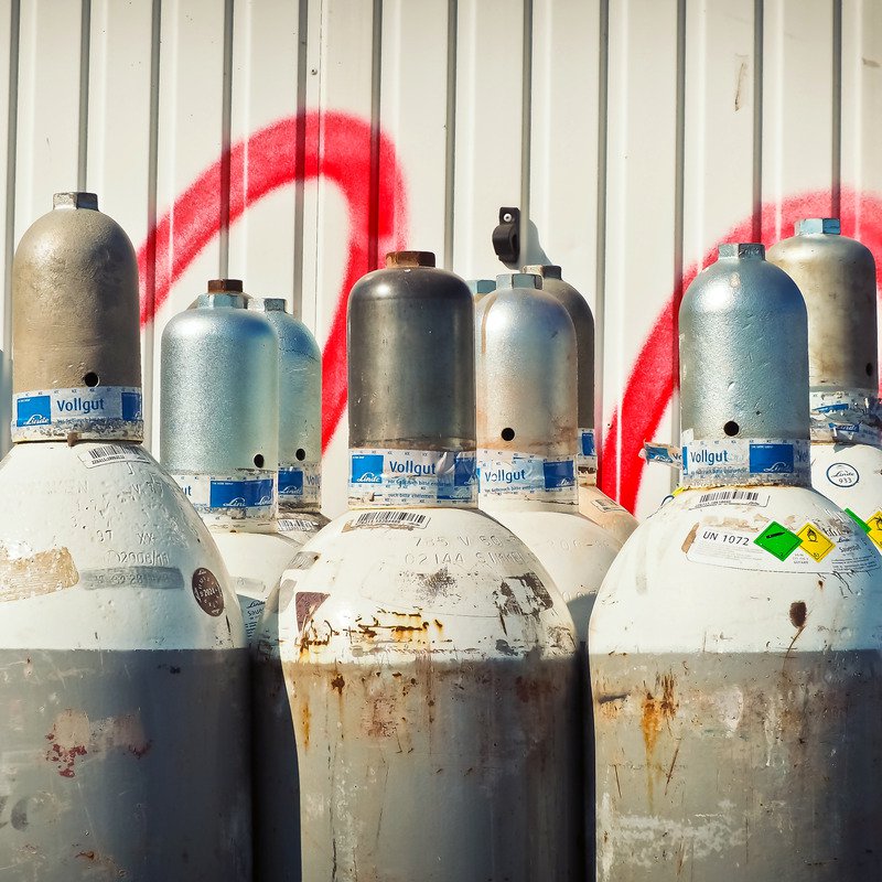 Gas bottles against a white wall with red paint on it.
