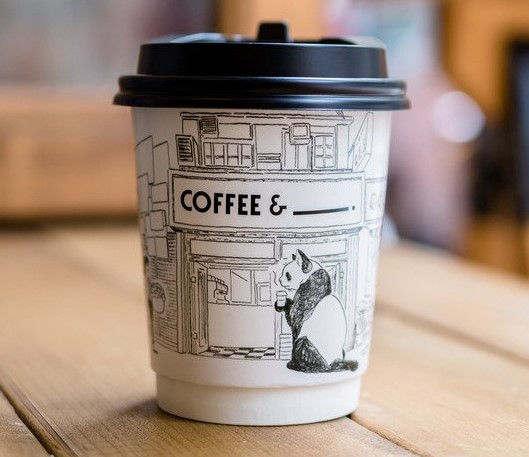 A paper coffee cup with a black lid and white body with a panda on it.