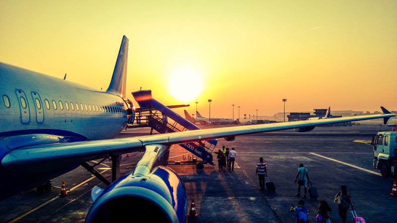 One side of an airplane with people queuing to get it on it, with a sunset in the background.