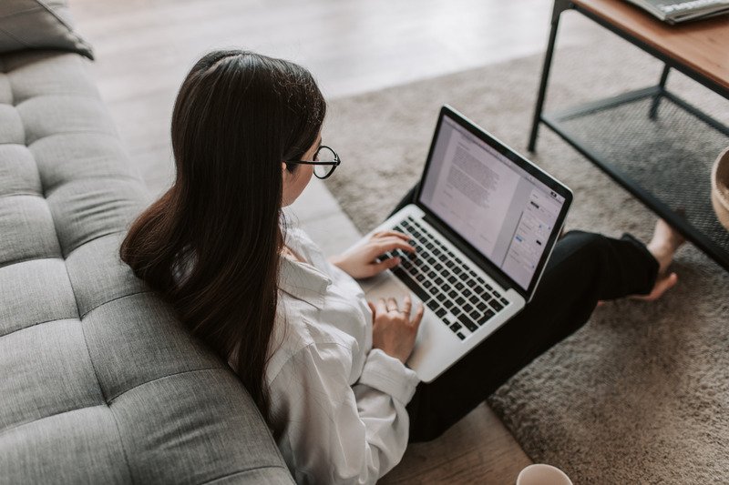 A woman sat on the floor in a living room on a laptop.