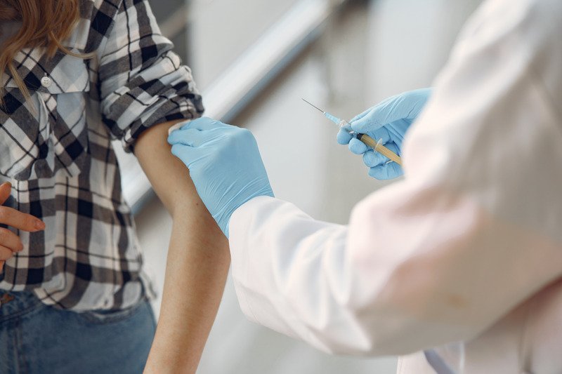 A medical professional wearing a white coat and blue gloves preparing to give someone a vaccination.