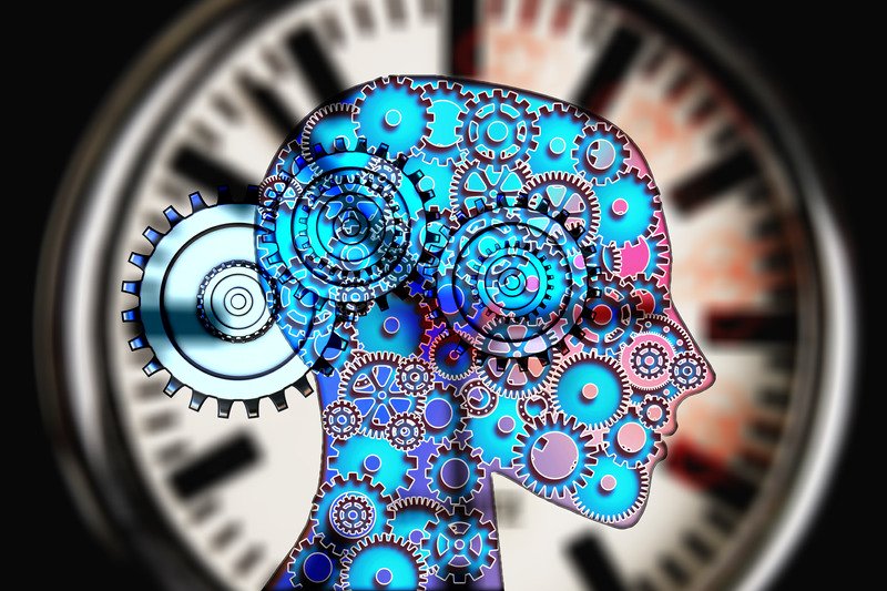 A human head with blue and pink cogs inside against a clock.
