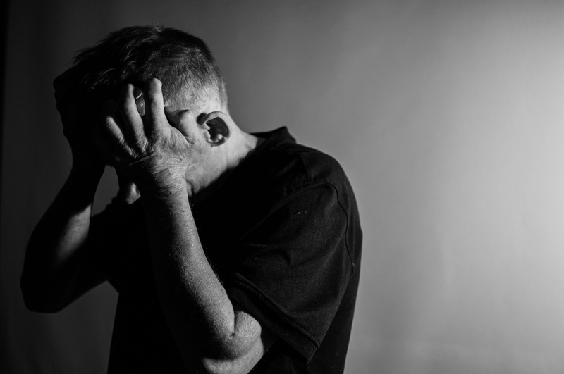 A black and white photo of a man looking stressed and holding his head in his hands.