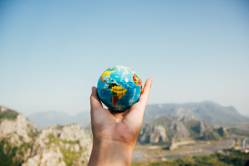 A an outreached hand holding a miniature globe facing a mountain.