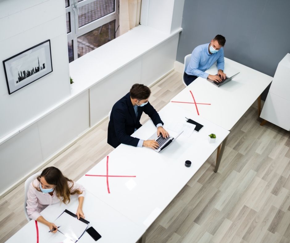 three people sat on a long desk, social distancing