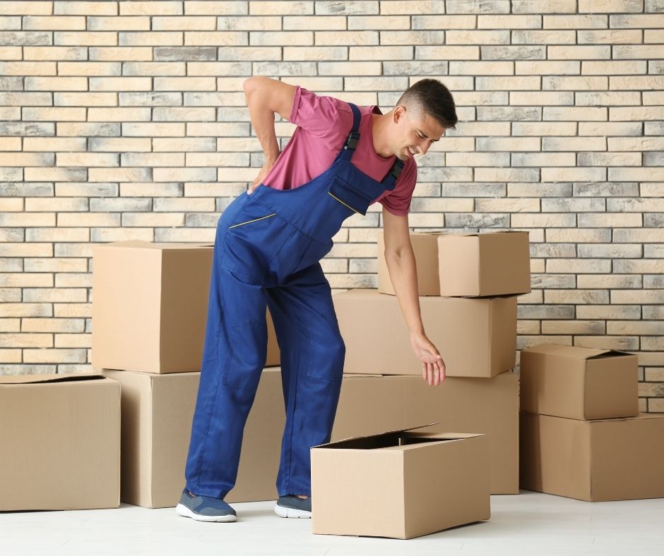 Man surrounded by cardboard boxes, hunched over holding his back in pain