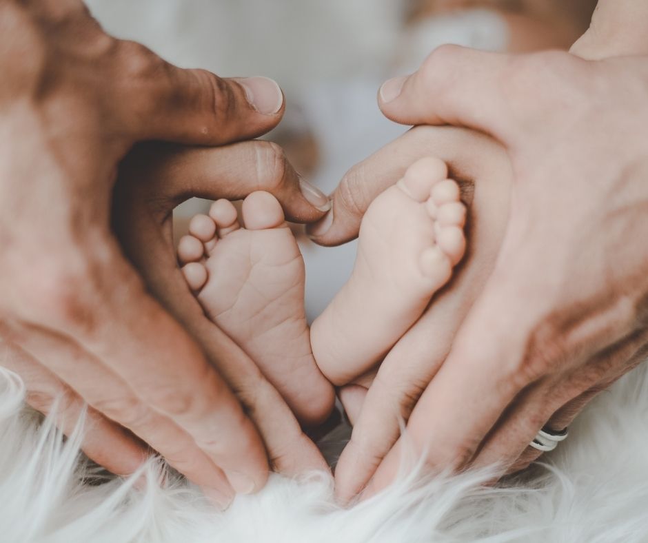 parents ands holding baby feet in a heart shape