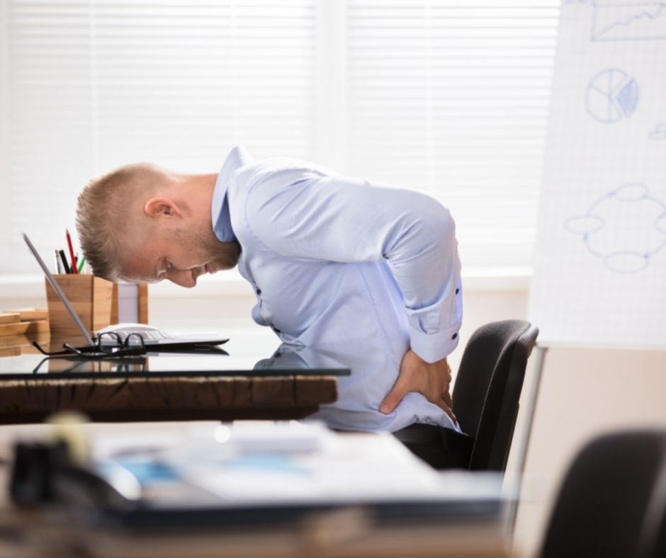 man at desk holding his back in pain