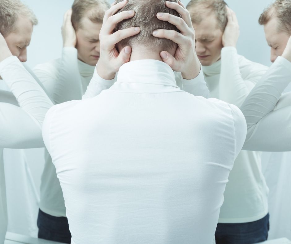 Person holding their head, seemingly in pain, in front of a number of mirrors