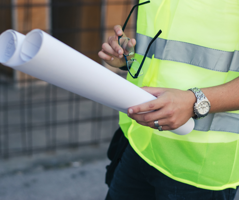 Person in a high vis holding a large rolled up sheet of paper