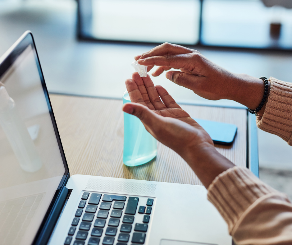 Close up of hands using hand sanitiser at a desk with a laptop