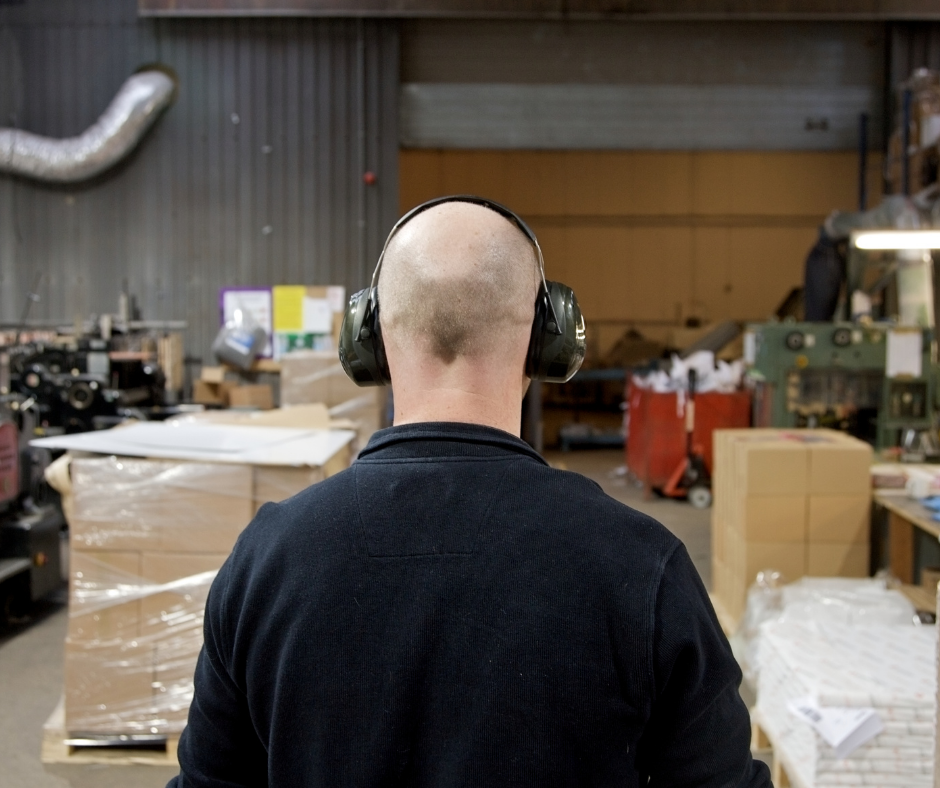 Bald man in warehouse wearing ear defenders