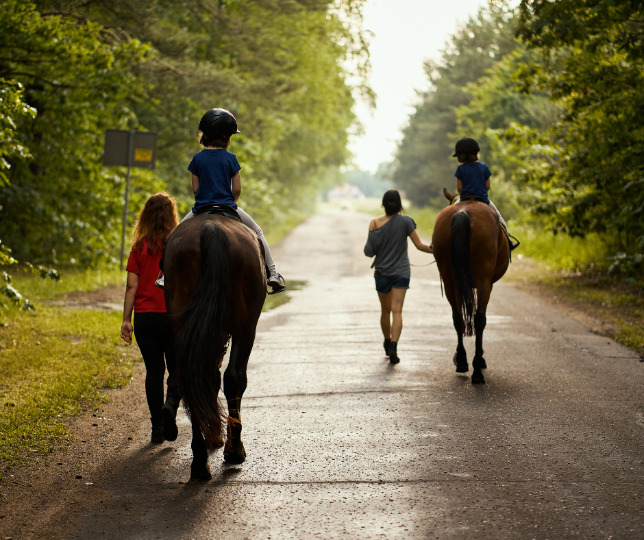 two children riding horses on the road with handlers