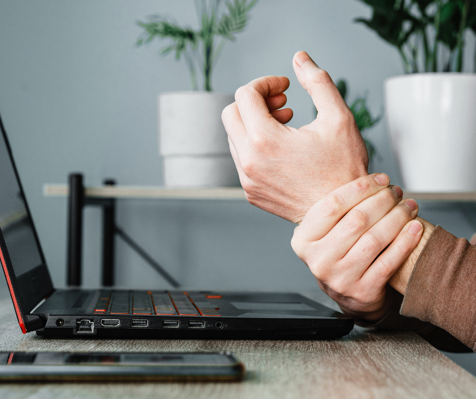 Someone holding their wrist in their other hand in front of a laptop