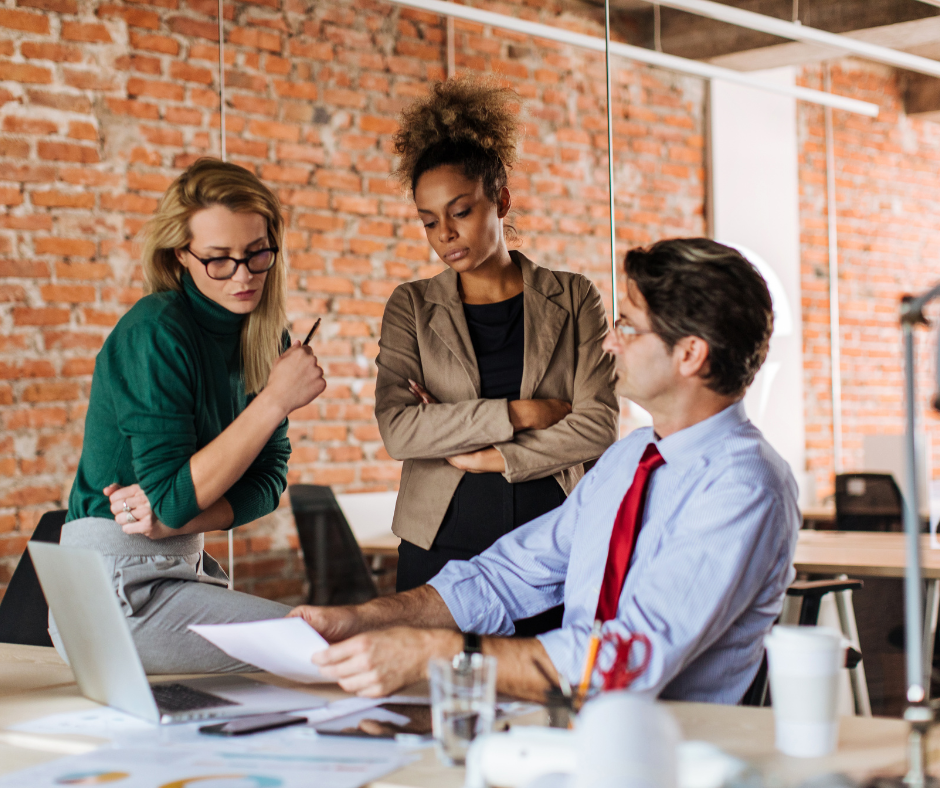 three colleagues discussing something at one colleague's desk